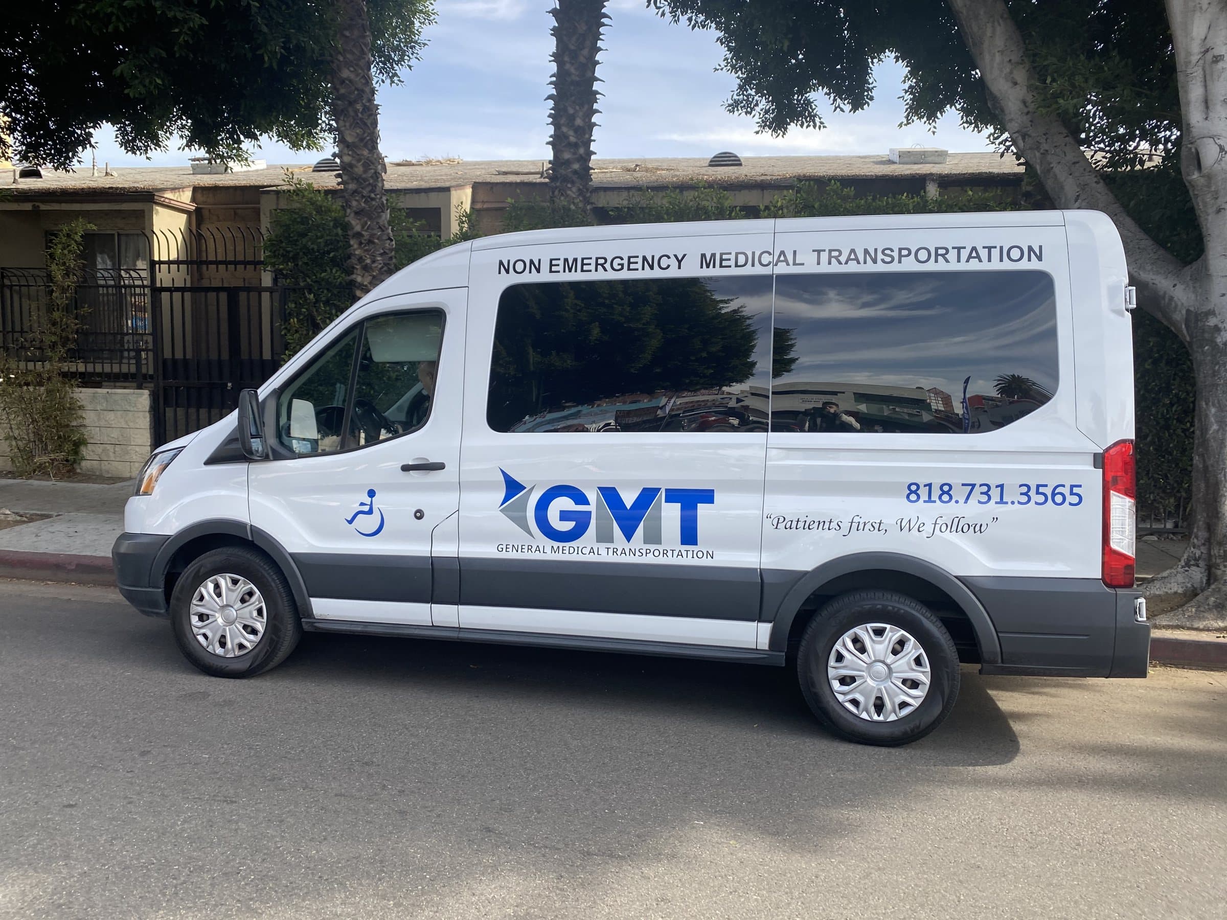 A white General Medical Transportation van marked Non Emergency Medical Transportation, with the GMT logo, a wheelchair symbol and the tagline "Patients first, We follow" on its side, parked on a tree-lined street.